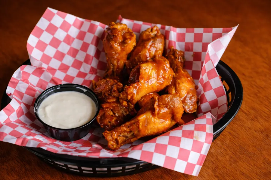 Basket of crispy golden fried chicken wings tossed in signature sauce